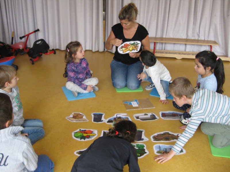  Erzieherin erklärt Kindern mit Bildkarten den Umgang mit Müll 
