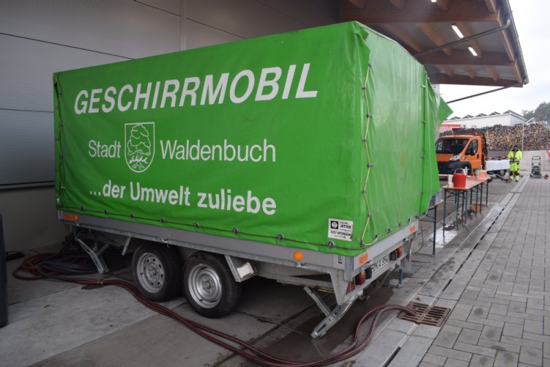 Grüner Anhänger mit der Aufschrift „Geschirrmobil Stadt Waldenbuch – der Umwelt zuliebe“ steht neben einem Gebäude.