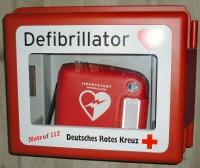 Defibrillator des Deutschen Roten Kreuzes (DRK) Rotes Defibrillator-Gerät in Wandkasten mit Aufschrift „Defibrillator – Deutsches Rotes Kreuz – Notruf 112“